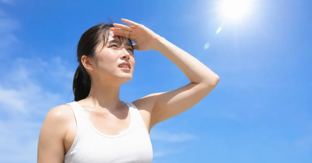 青空の炎天下で、女性が汗ばみながら、手で日光を遮ろうとしています。